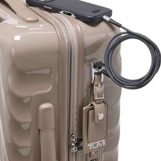 Beige Tumi suitcase with a security cable and device attached on a white background