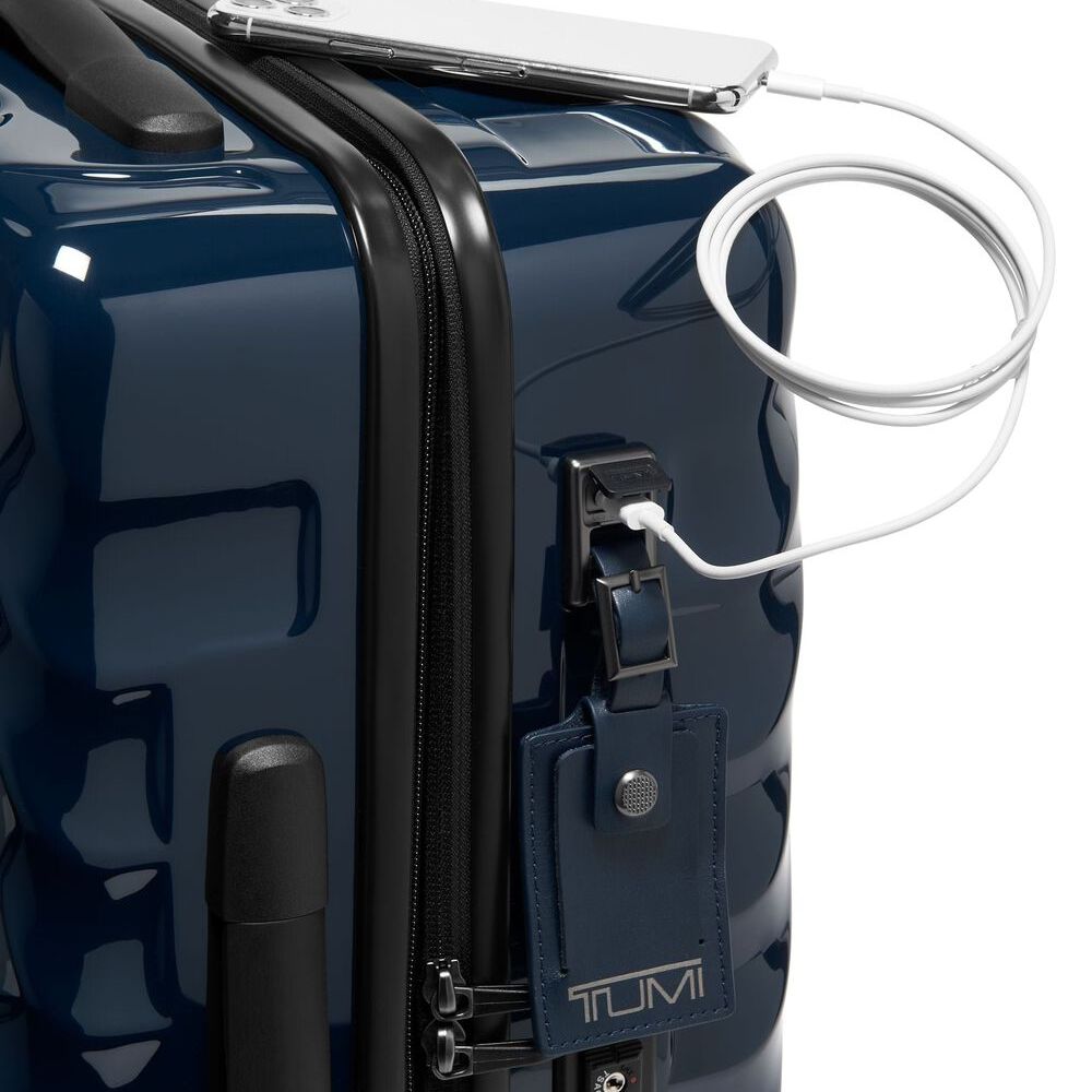 Navy blue Tumi suitcase with a white cable plugged into a USB port on a white background